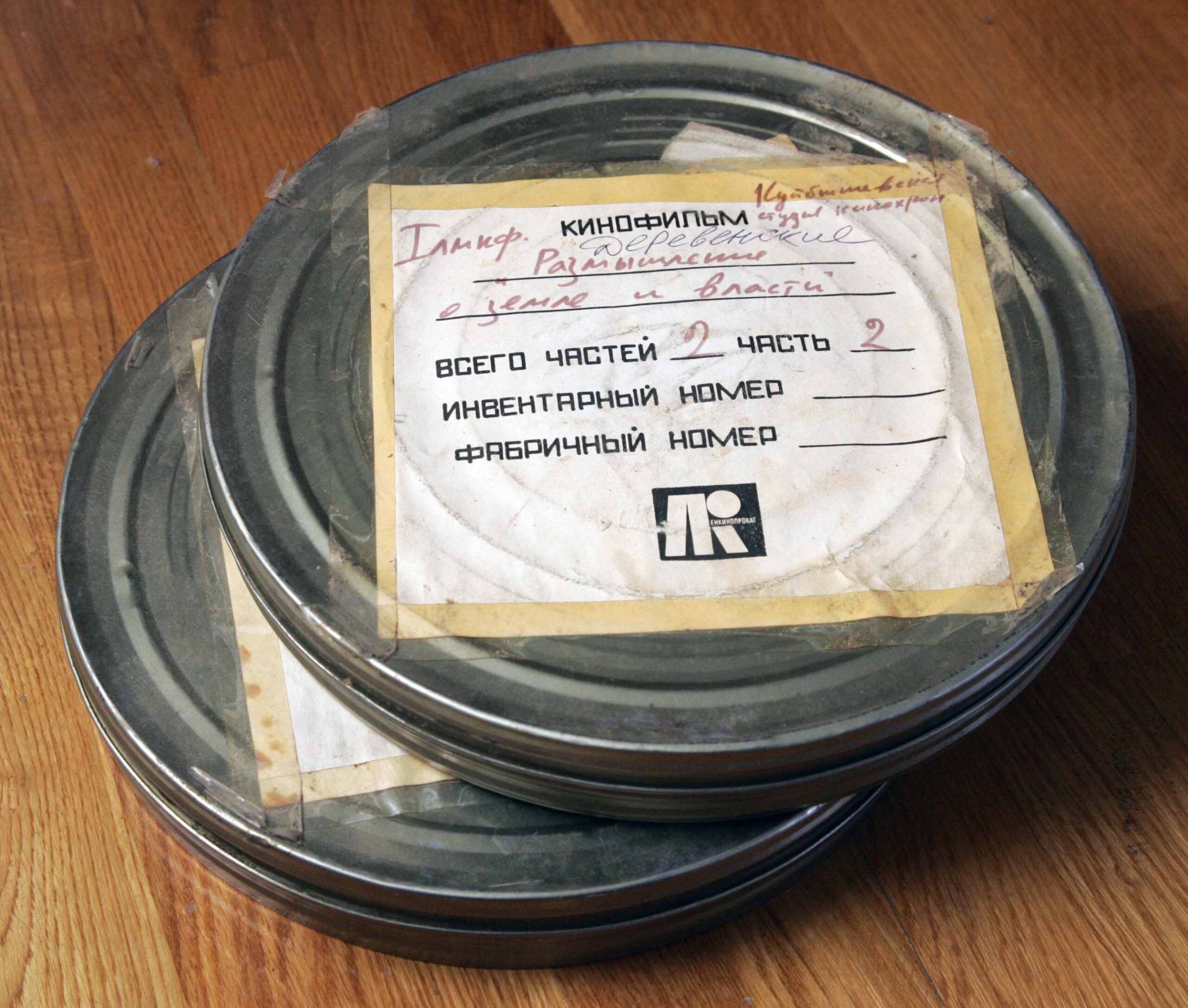 Two round metal film storage cans stacked on a wooden surface with a paper label on top.
