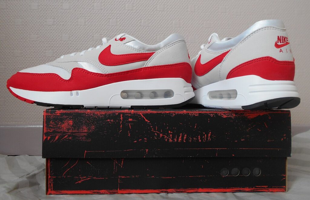 Red-and-white Nike Air Max 1 trainers on a shoebox, with the transparent cushioning windows visible.