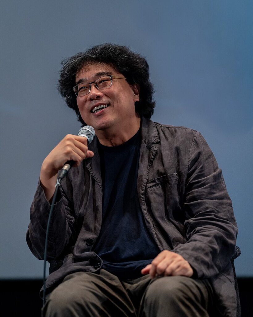 Bong Joon-ho smiling and holding a microphone at the 2025 Busan International Film Festival.