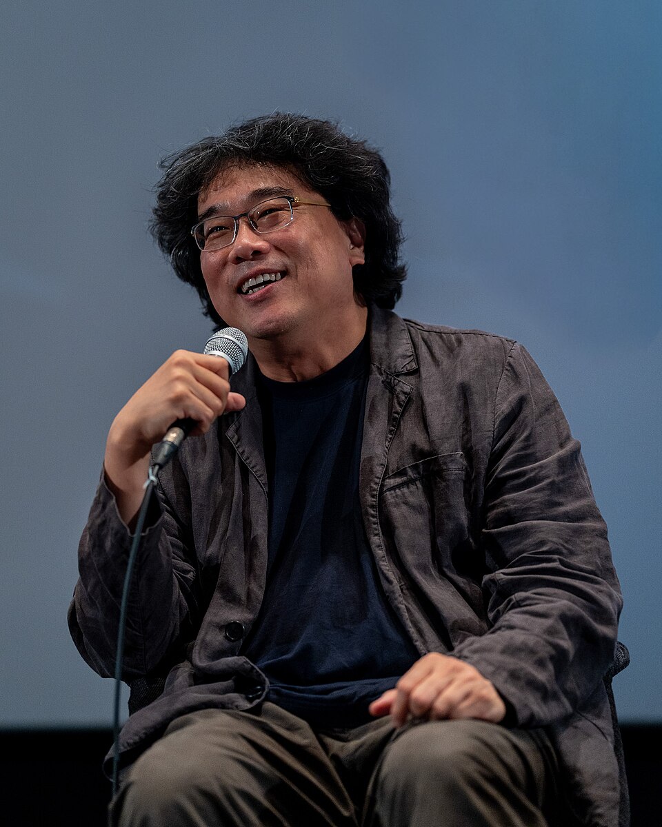 Bong Joon-ho smiling and holding a microphone at the 2025 Busan International Film Festival.